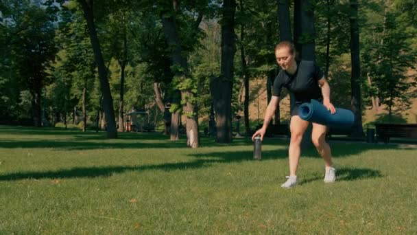 jong sportvrouw meisje houdt karemat en fles water in handen voordat training buiten in het park zet mat op gras gezonde levensstijl concept - Video