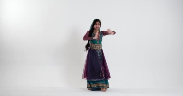 Uma jovem mulher indiana dança no fundo branco energeticamente à música tradicional, vestida com um sari colorido com tons azuis, roxos e verdes, e adornada com jóias tradicionais indianas.. - Filmagem, Vídeo