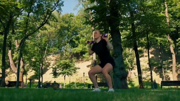 портрет молодої задоволеної спортивної дівчини, яка виконує вправи з гантелями на відкритому повітрі під час тренування в парку концепція здорового способу життя - Кадри, відео
