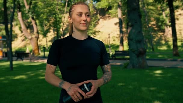 portrét mladé spokojené sportovní dívka házení láhev vody do nebe venku po cvičení v parku zdravý životní styl koncept - Záběry, video