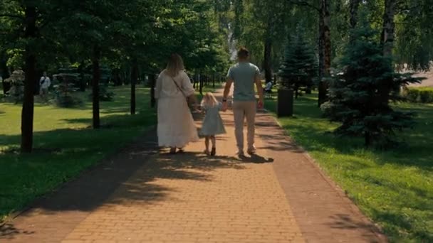 Little cute girl w zielonej sukni letniej z rodzicami w parku miejskim na spacer lato rodzinny styl życia - Materiał filmowy, wideo