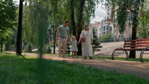 Pequena menina bonito no vestido de verão verde com os pais no parque da cidade na caminhada verão estilo de vida familiar Infância feliz família de mãos dadas - Filmagem, Vídeo