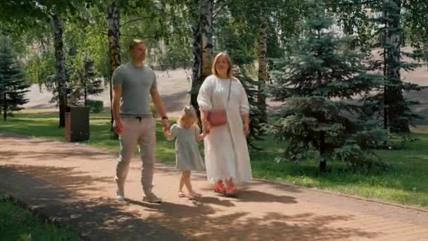 Pequena menina bonito no vestido de verão verde com os pais no parque da cidade na caminhada verão estilo de vida familiar Infância feliz família de mãos dadas - Filmagem, Vídeo