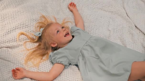 портрет щасливої дівчини, що лежить на ковдрі в парку Мрійливе обличчя дитини дитина дивиться на небо Посмішка дитинство вид зверху - Кадри, відео
