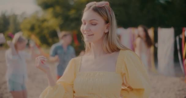Piękna młoda blondynka grooving przeciwko przyjaciołom tańczącym na plaży w letni weekend - Materiał filmowy, wideo