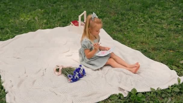 Parkta elbise giymiş şirin bir kız keçeli kalemle ailesini gösteren bir kartpostal çizmiş. - Video, Çekim