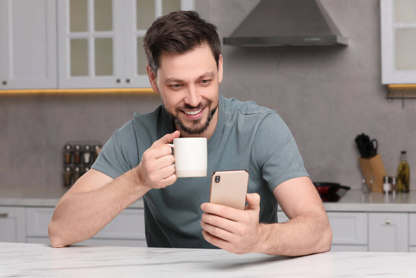 Ο άνθρωπος που χρησιμοποιεί το smartphone, ενώ το πρωινό στο τραπέζι στην κουζίνα. Εθισμός στο Διαδίκτυο - Φωτογραφία, εικόνα