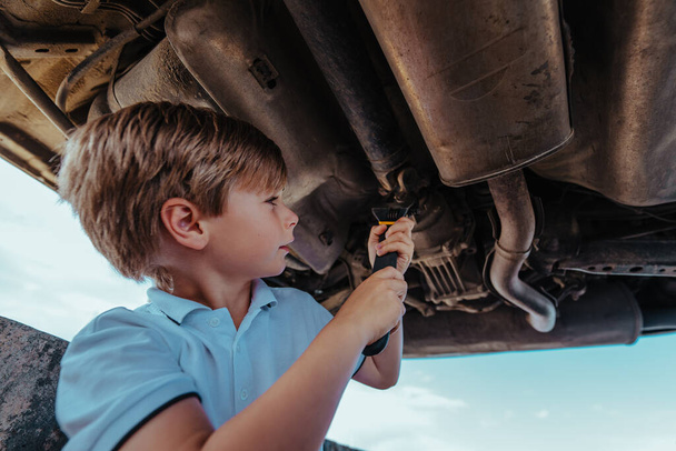 Boy automotive mechanic standing under car bottom with wrench and repairing car - Photo, Image