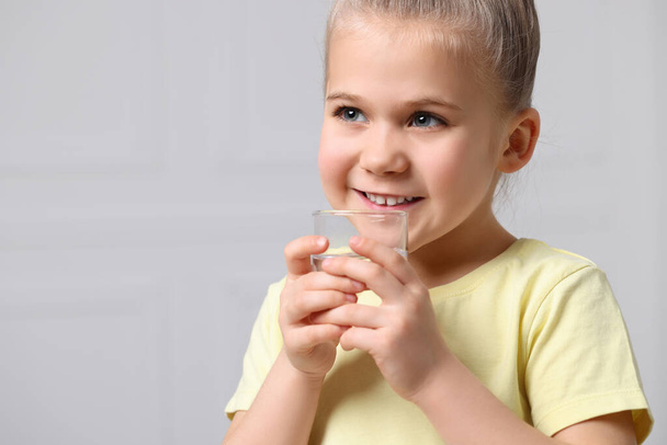 Happy little girl holding glass of fresh water on grey background, space for text - Foto, afbeelding