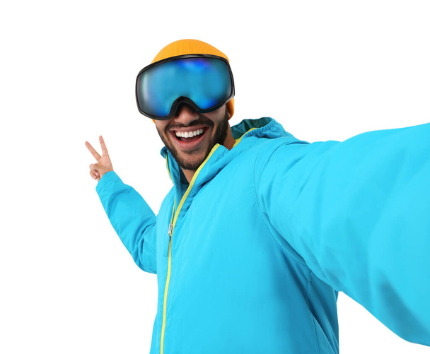 Lächelnder junger Mann mit Skibrille macht Selfie und zeigt Friedenszeichen auf weißem Hintergrund - Foto, Bild