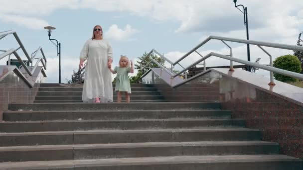 Kicsi aranyos lány zöld nyári ruhában masnival sétálni a terhes anyjával a parkban gyerekkori családi nyaralás anyák napja - Felvétel, videó