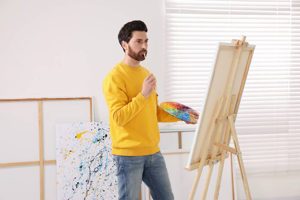 Man painting in studio. Using easel to hold canvas - Фото, изображение