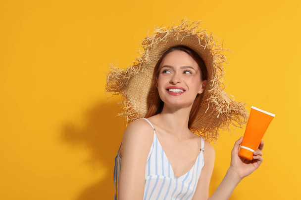 Beautiful young woman in straw hat holding sun protection cream on orange background, space for text - Valokuva, kuva