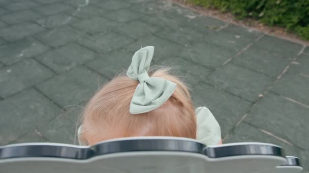 Pieni söpö tyttö vihreässä kesämekossa, jossa on jousi leikkikentällä yksin nauraen hymyilevä lapsuuden lapsi ilman aikuisen valvontaa - Materiaali, video
