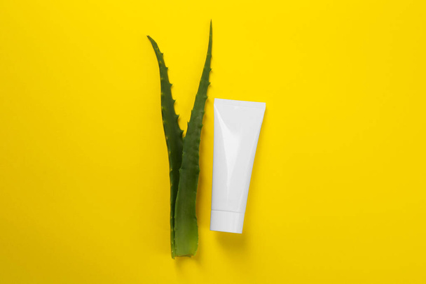 Aloe vera toothpaste in blank tube and green leaves on yellow background, flat lay. Space for text - Photo, Image