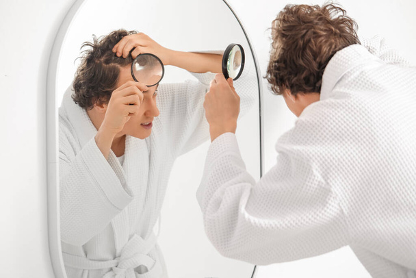 Young man magnifying his hair near mirror in bathroom - Valokuva, kuva