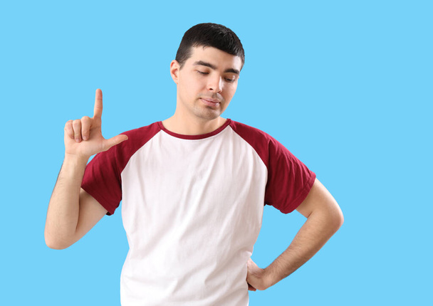 Verontruste jongeman toont verliezer gebaar op blauwe achtergrond - Foto, afbeelding