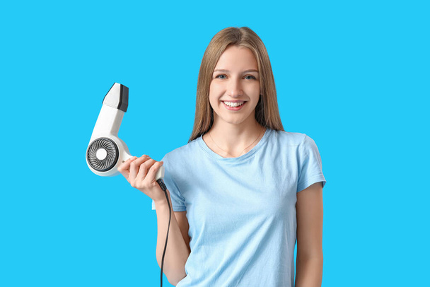 Beautiful young woman with hair dryer on light blue background - Fotografie, Obrázek