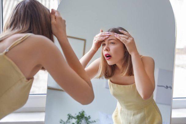 Giovane donna schiacciamento brufolo davanti allo specchio a casa - Foto, immagini