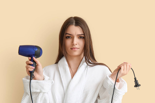 Displeased young woman with hair dryer on beige background - Valokuva, kuva