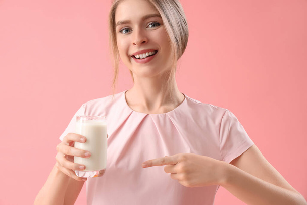 Young woman pointing at tasty yoghurt on pink background, closeup - 写真・画像