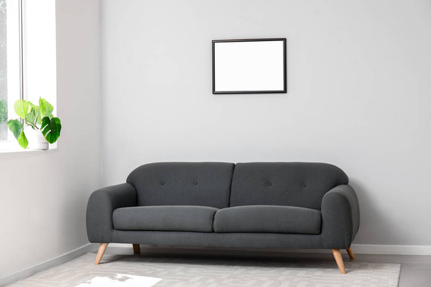 Interiér světlého obývacího pokoje s útulnou šedou pohovkou, pokojovou rostlinou na parapetu a prázdným rámečkem - Fotografie, Obrázek
