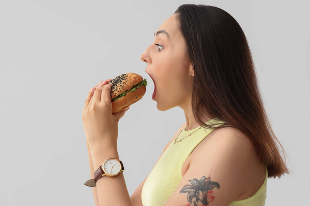 Junge Frau isst leckeren Burger auf hellem Hintergrund, Nahaufnahme - Foto, Bild