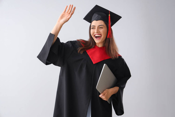 Female graduate student with laptop on light background - Foto, imagen