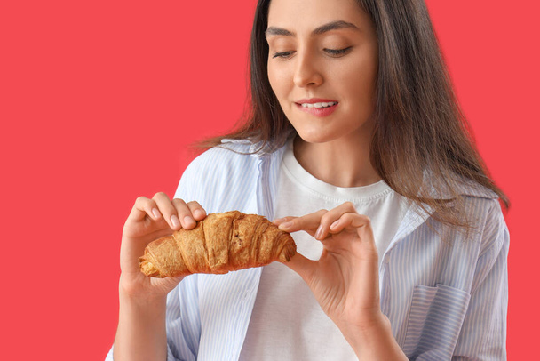 Young woman with tasty croissant on red background, closeup - Fotoğraf, Görsel