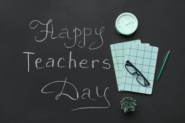 Notitieboekjes met wekker, bril en tekst HAPPY TEACHERS DAY on black chalkboard - Foto, afbeelding