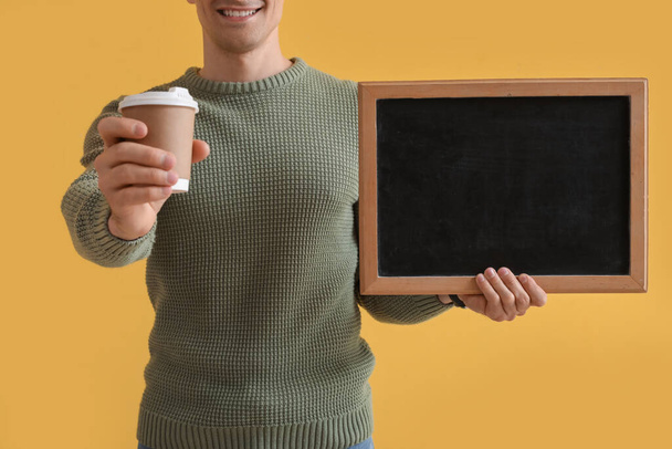 Profesor masculino con pizarra y taza de café sobre fondo amarillo, primer plano - Foto, Imagen