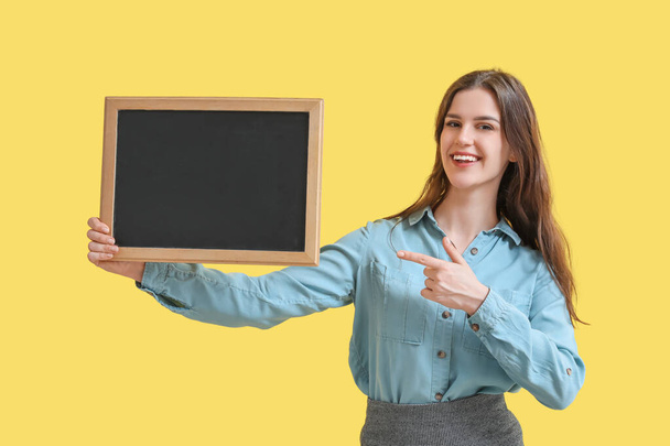 Female teacher pointing at chalkboard on yellow background - Zdjęcie, obraz