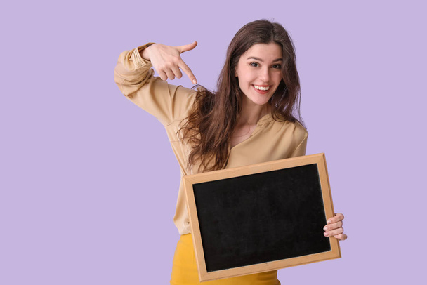 Female teacher pointing at chalkboard on lilac background - Photo, Image