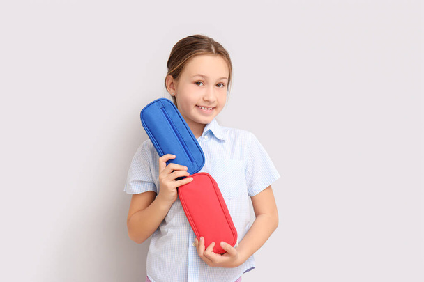 Little girl with pencil cases on light background - 写真・画像
