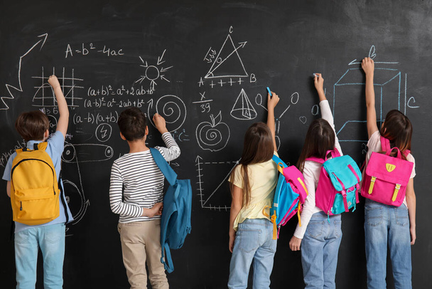 Little pupils with backpacks near blackboard, back view - Фото, изображение