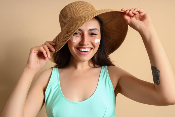 Young woman with sunscreen cream on beige background, closeup - Foto, afbeelding