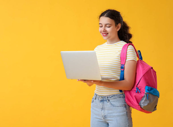 Female student with laptop and backpack on yellow background - Fotoğraf, Görsel