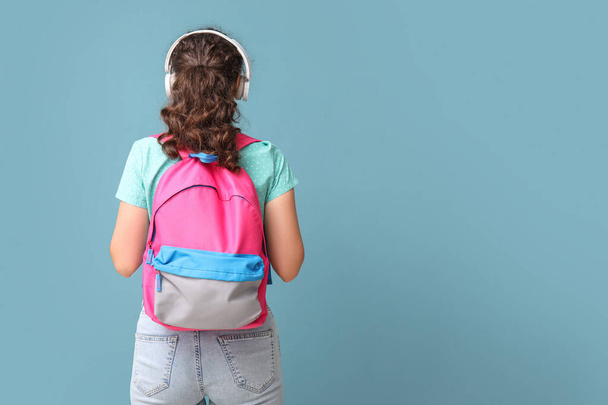 Female student in headphones with backpack on blue background, back view - Fotoğraf, Görsel