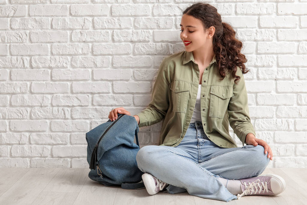 Female student with backpack sitting near white brick wall - Foto, Bild