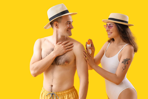 Junges Paar cremt Sonnencreme auf gelbem Hintergrund ein - Foto, Bild