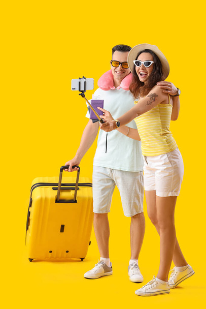 Young couple with passports and suitcase taking selfie on yellow background - Photo, Image