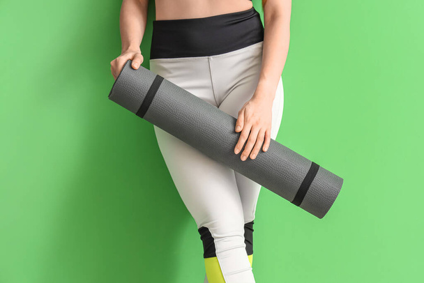 Junge Frau in Sportbekleidung und mit Yogamatte auf grünem Hintergrund - Foto, Bild