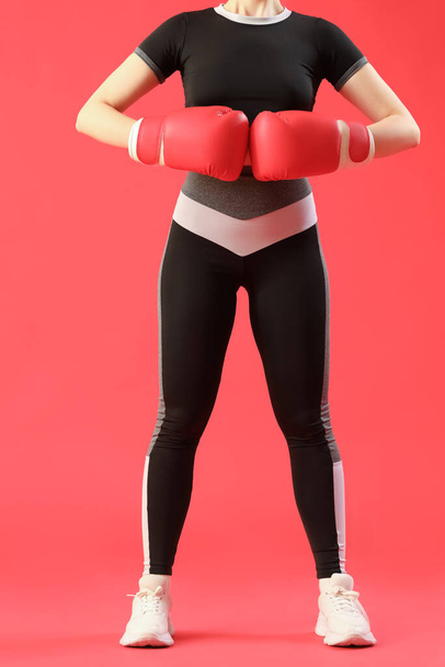 Νεαρή γυναίκα με αθλητικά ρούχα και γάντια πυγμαχίας σε κόκκινο φόντο - Φωτογραφία, εικόνα