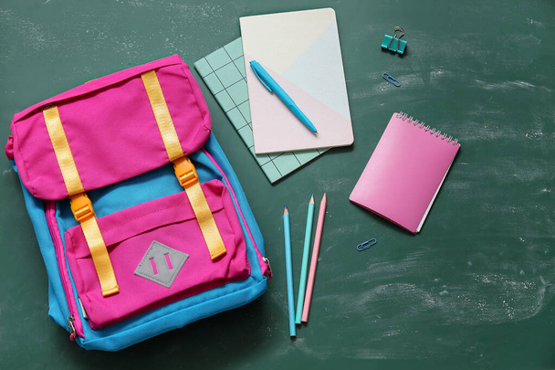 Барвистий шкільний рюкзак з блокнотами, ручкою та олівцями на зеленому фоні - Фото, зображення