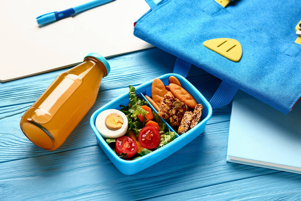 Batoh, papírnictví a občerstvení s chutným jídlem na modrém dřevěném pozadí - Fotografie, Obrázek