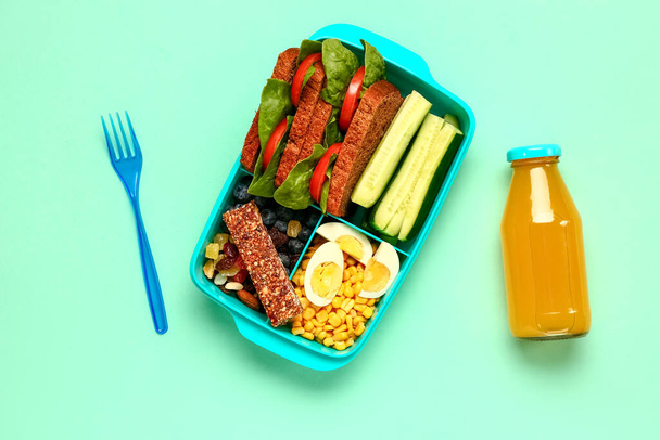 Bottle of juice, fork and lunchbox with tasty food on turquoise background - Photo, Image
