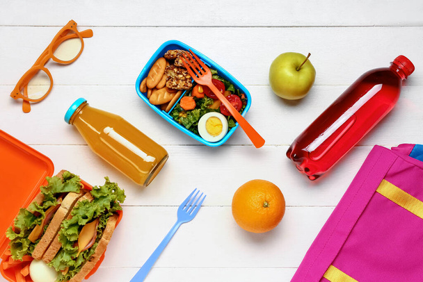 Bouteilles de jus, sac à dos et boîtes à lunch avec des aliments savoureux sur fond de bois blanc - Photo, image