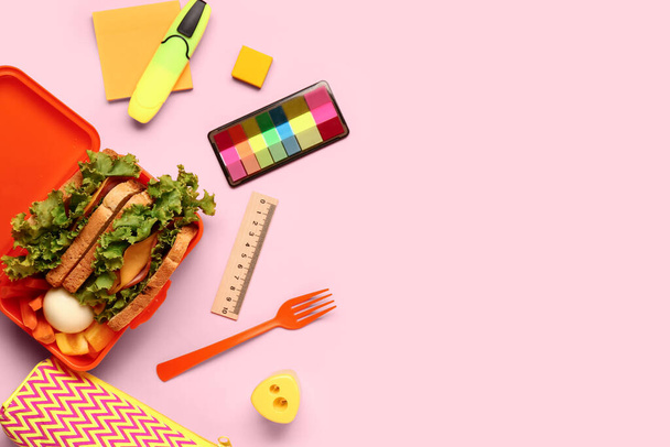 Канцелярські товари та обідня коробка зі смачною їжею на рожевому фоні - Фото, зображення