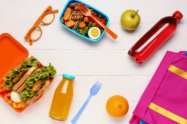Frame made of juices, backpack and lunchboxes with tasty food on white wooden background - Foto, Imagem