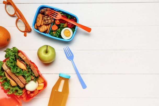 Butelka soku, okularów, owoców i pudełek śniadaniowych ze smacznym jedzeniem na białym drewnianym tle - Zdjęcie, obraz